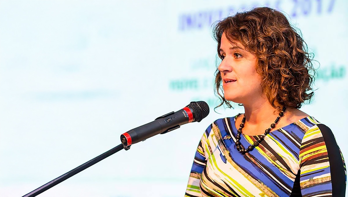 A woman with a multi-coloured shirt speaks into a microphone.