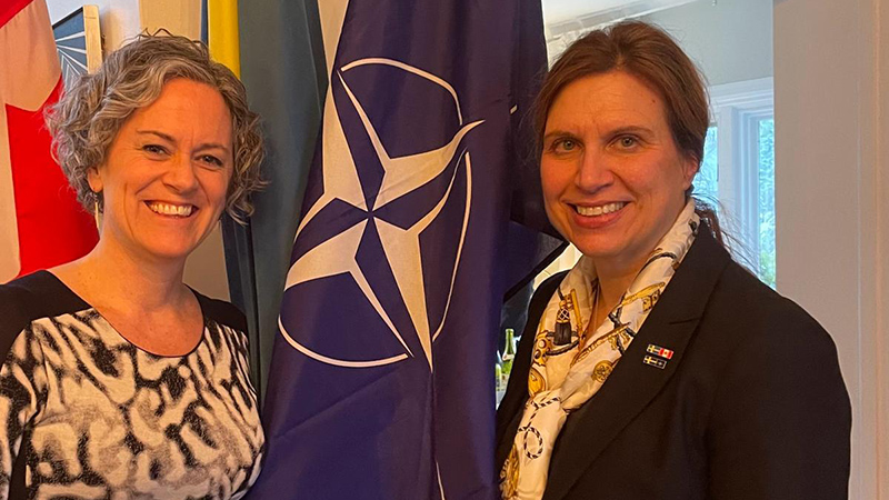 Two women - the ambassador of Canada to Austria, and the ambassador of Sweden to Austria - posing with various flags.