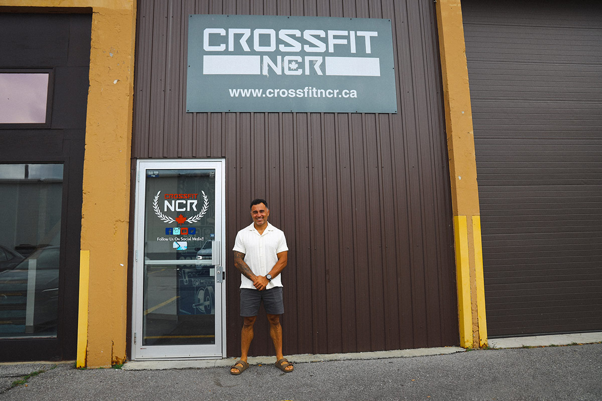 Reza Mashkoori stands outside the CrossFit NCR facility, wearing casual summer clothes in front of the gym’s entrance.