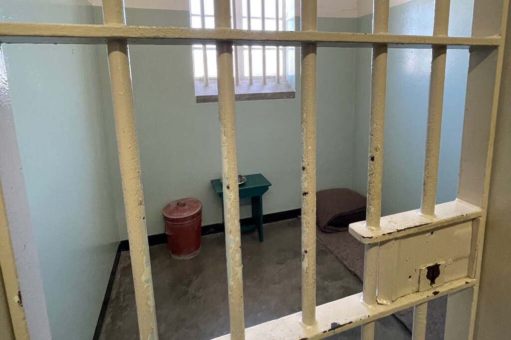 A photo of inside an old jail cells, taken from outside of the cell.