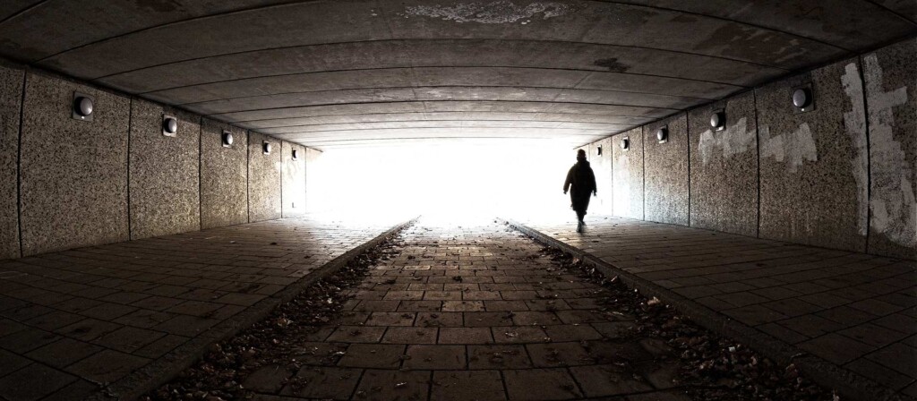 A silhouette of a person walking though a dark tunnel on a ghost walk, symbolizing dark tourism.