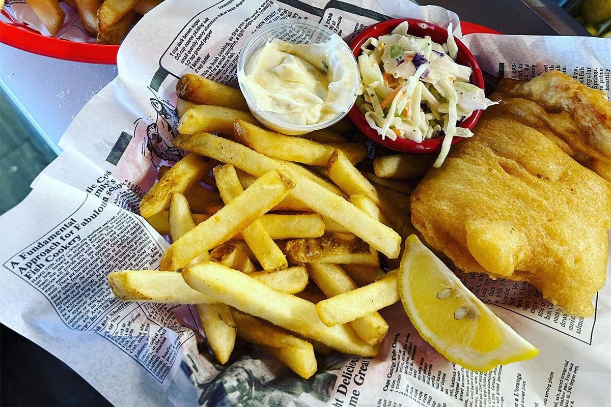 Fish and chips with a slice of lemon and coleslaw salad.