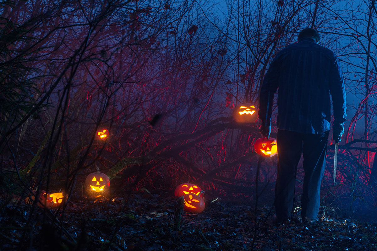 Man with pumpkin and knife in dark forest of glowing jack-o’-lanterns — symbolizing Indigenous stereotypes and modern horror.