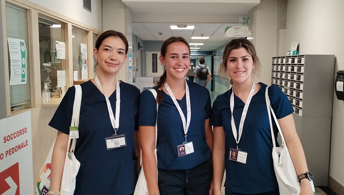 Three health sciences students posing for a group photo inside a hospital while wearing scrubs.