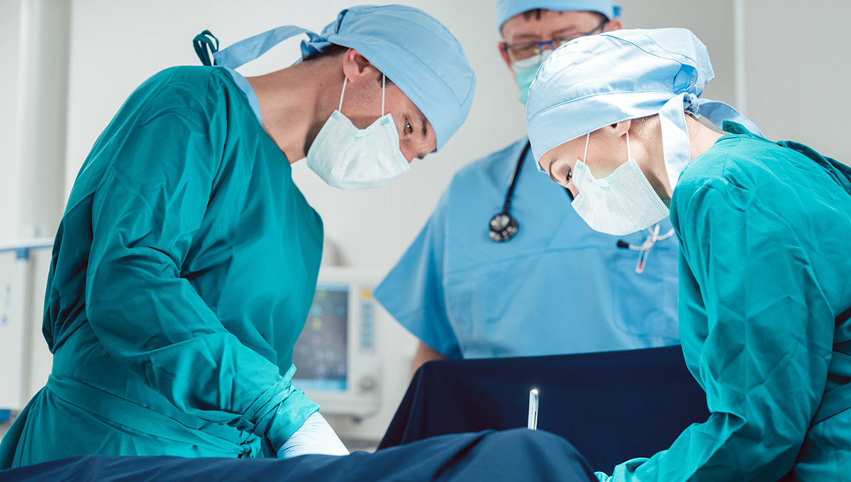 Three doctors working in an operating room working on a patient.