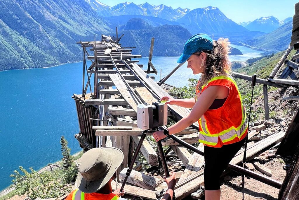 Two researchers use a 3D laser scanner to document a deteriorating wooden railway structure.