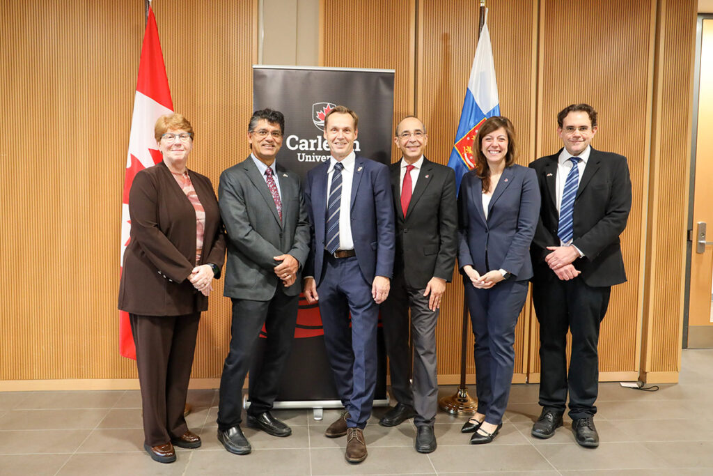 Five people posing for a group photo in front of the flags of Canada and Finland.
