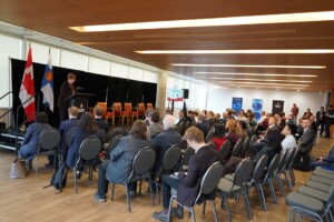 A woman addresses a seated audience from a podium.