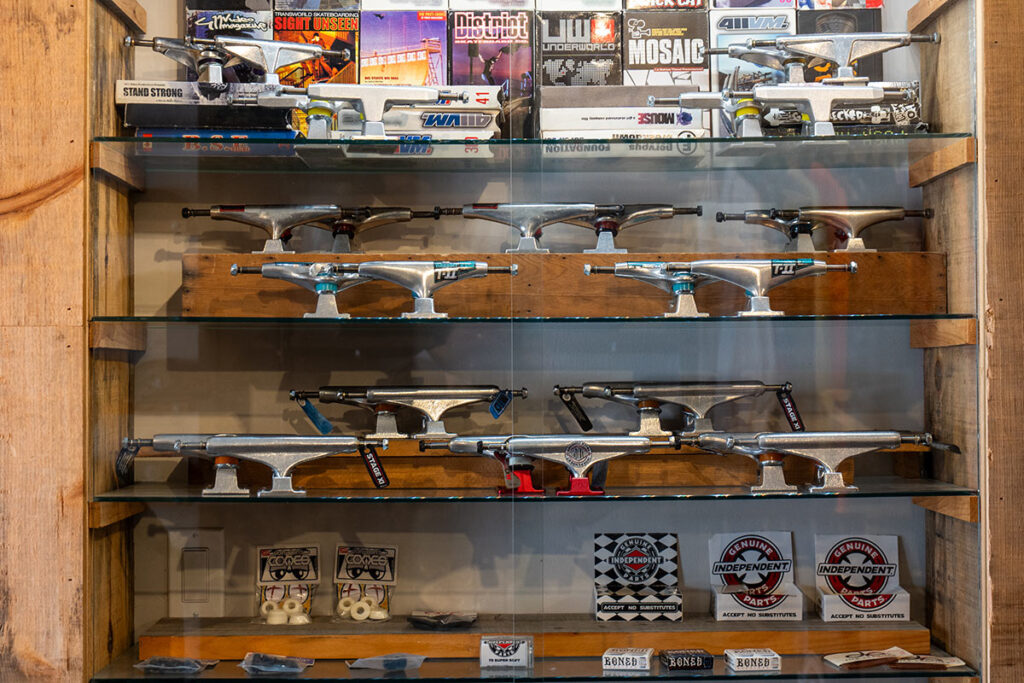 A glass display case showing various skateboard trucks, wheels, and parts from brands like Independent and Bones.
