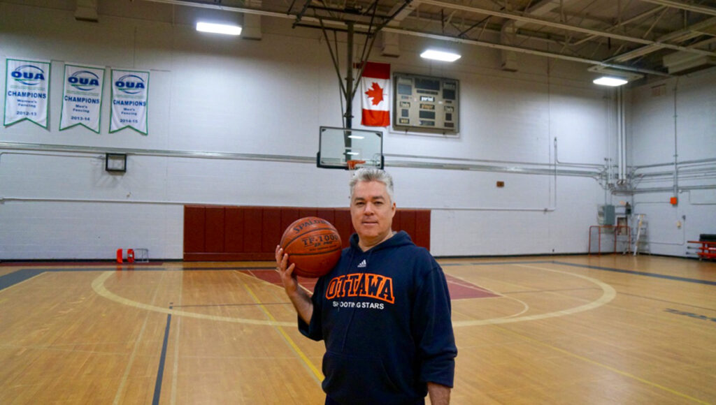 A man holds a basketball while standing on a basketball court.