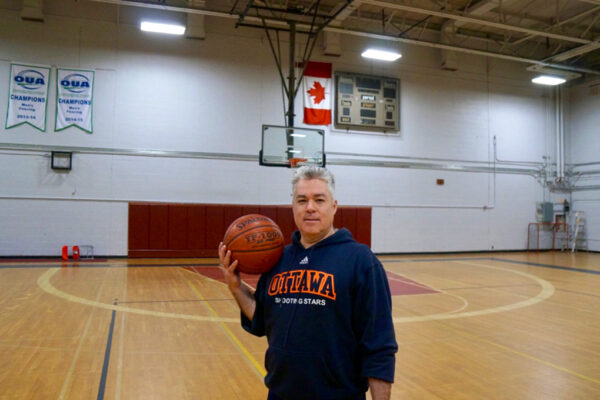 A man holding a basketballs stands on a basketball court.