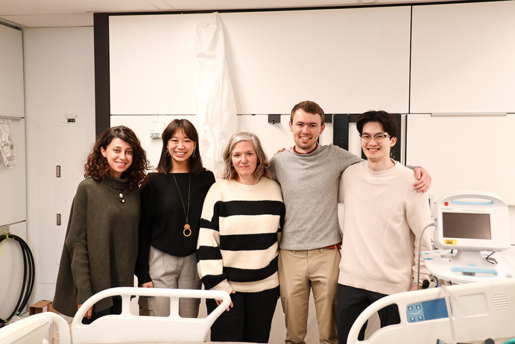 Five people posing for a group photo inside a classroom.