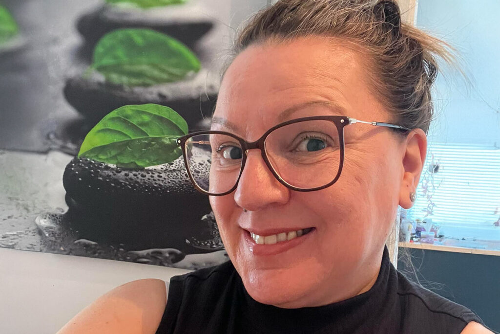 A woman wearing glasses and a black shirt smiles for the camera.