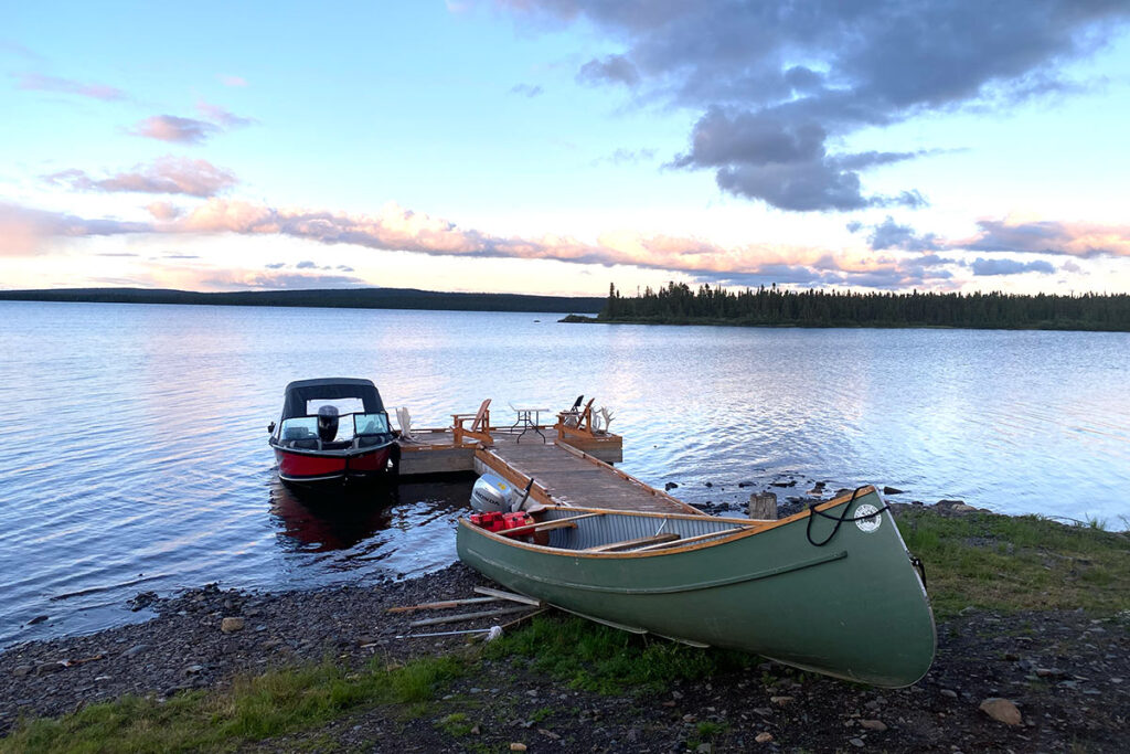 A canoe on the shore with a wooden dock and lake in the background.