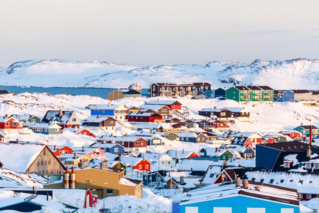 Lots of Inuit houses scattered on the hill in Nuuk city covered in snow with sea and mountains in the background, in Greenland.