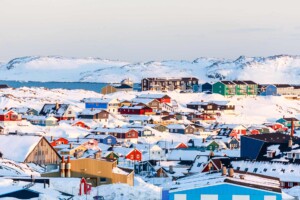 Lots of Inuit houses scattered on the hill in Nuuk city covered in snow with sea and mountains in the background, in Greenland.
