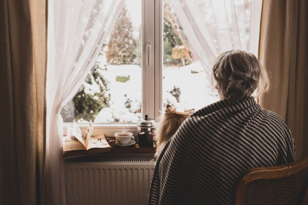 Person sitting by a window looking out at a snowy winter scene, reflecting the quiet isolation often associated with Blue Monday.