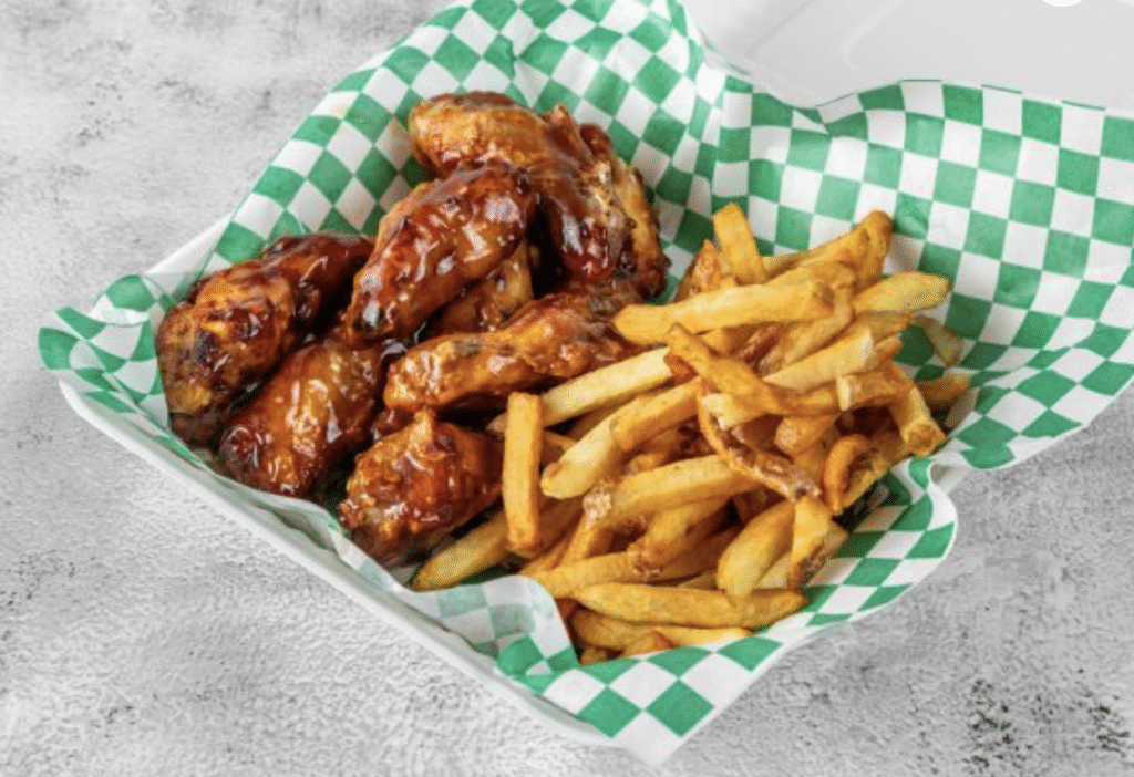 A restaurant serving of hot wings and French fries nestled in parchment paper.