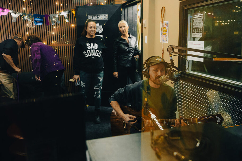 A guitar player performs inside the CKCU Radio studio with onlookers.