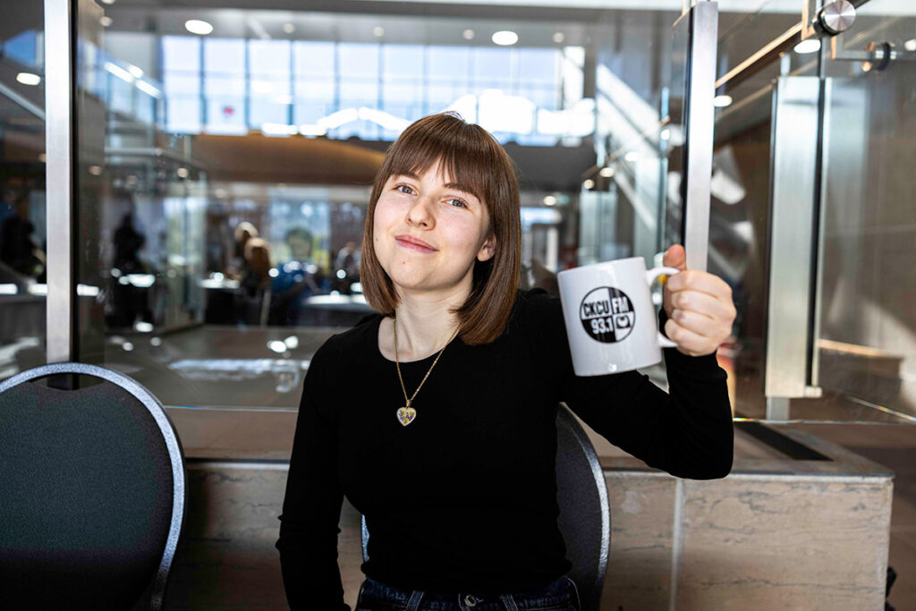 A woman in a black shirt holds up a white mug with the CKCU logo.