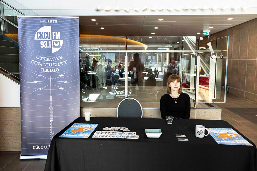 A young woman sits at a promotional booth during a conference event.