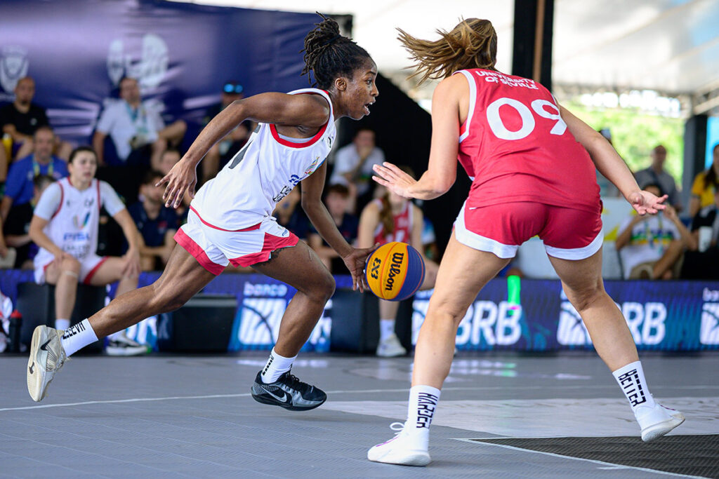 Dorcas Buisa dribbles past a defender in a competitive outdoor basketball game while attacking the basket.