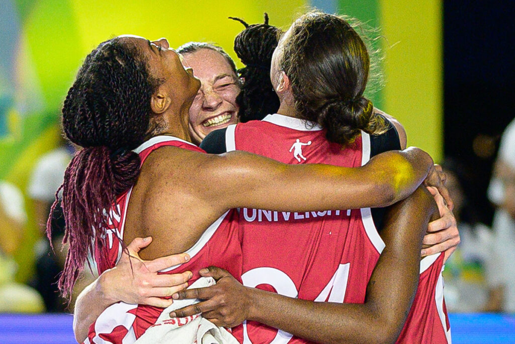 Four basketball players celebrate winning a game while standing on a basketball court.