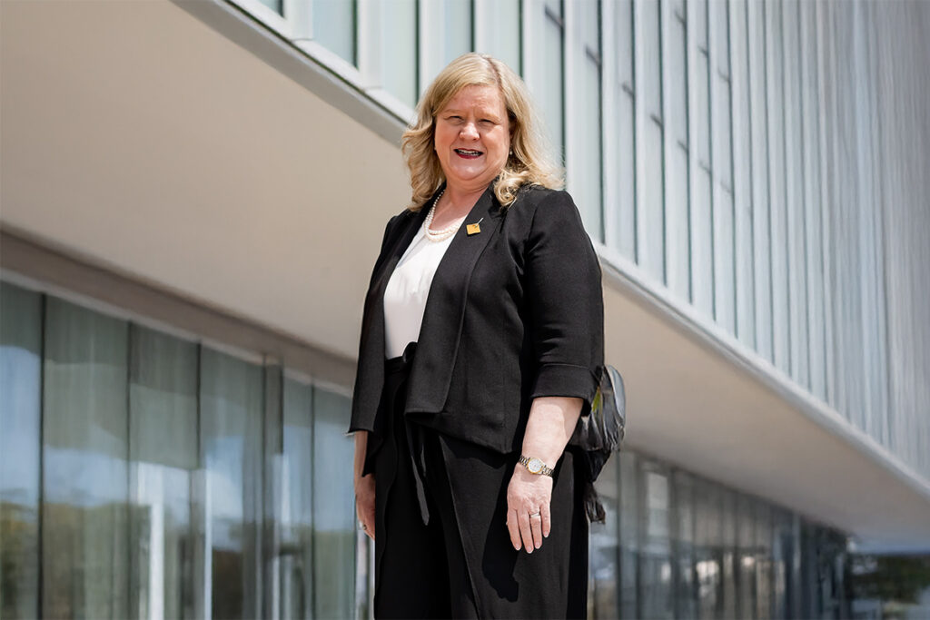 A woman wearing a dark suit and white shirt poses for a photo in front of an office building.