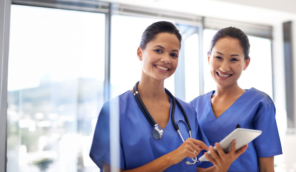 Two nurses looking at a chart and smiling for a the camera.