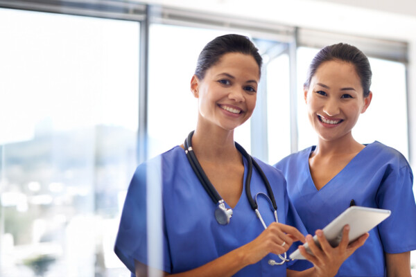 Two nurses looking at a chart and smiling for a the camera.