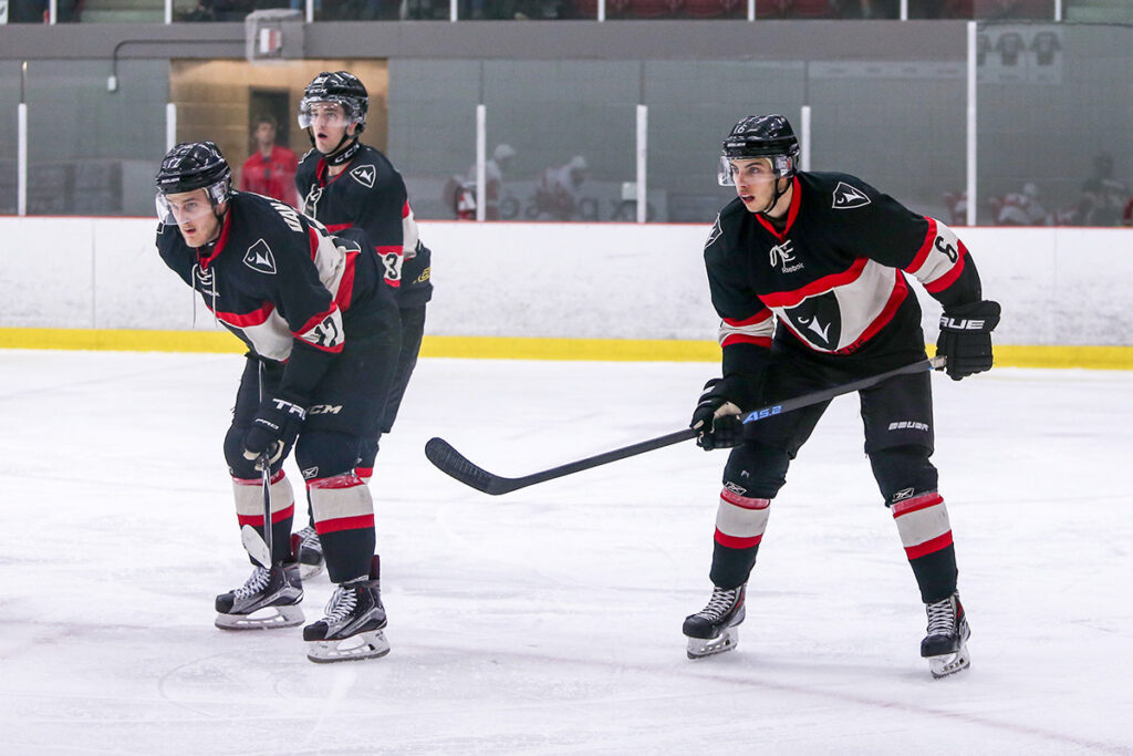Three hockey players lining up for a face off during a university level game.