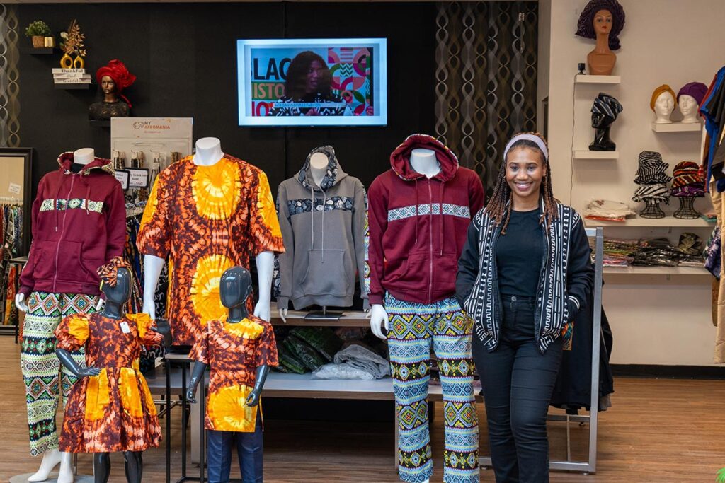 A woman stands next to mannequins in front of a clothing store.