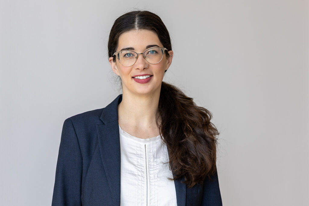 A woman with glasses, wearing a blue blazer, poses for a professional headshot.