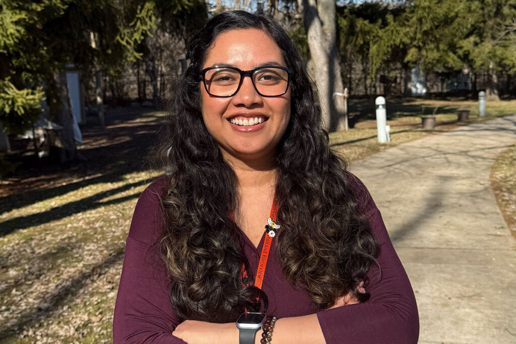 A woman smiles for the camera outside while crossing her arms.