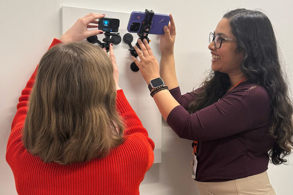 Two women holding up cameras to a poster attached to a wall.