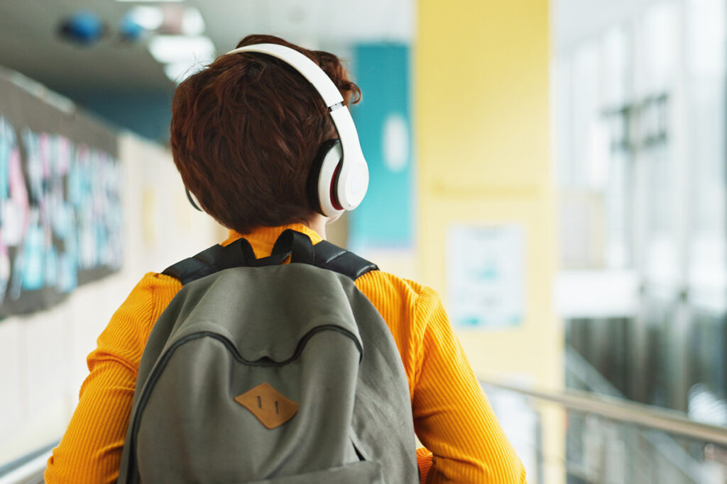 The back of a child walking in a school while wearing a backpack and headphones.