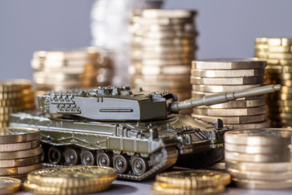 A toy tank surrounded by coins, representing an increase in military spending.