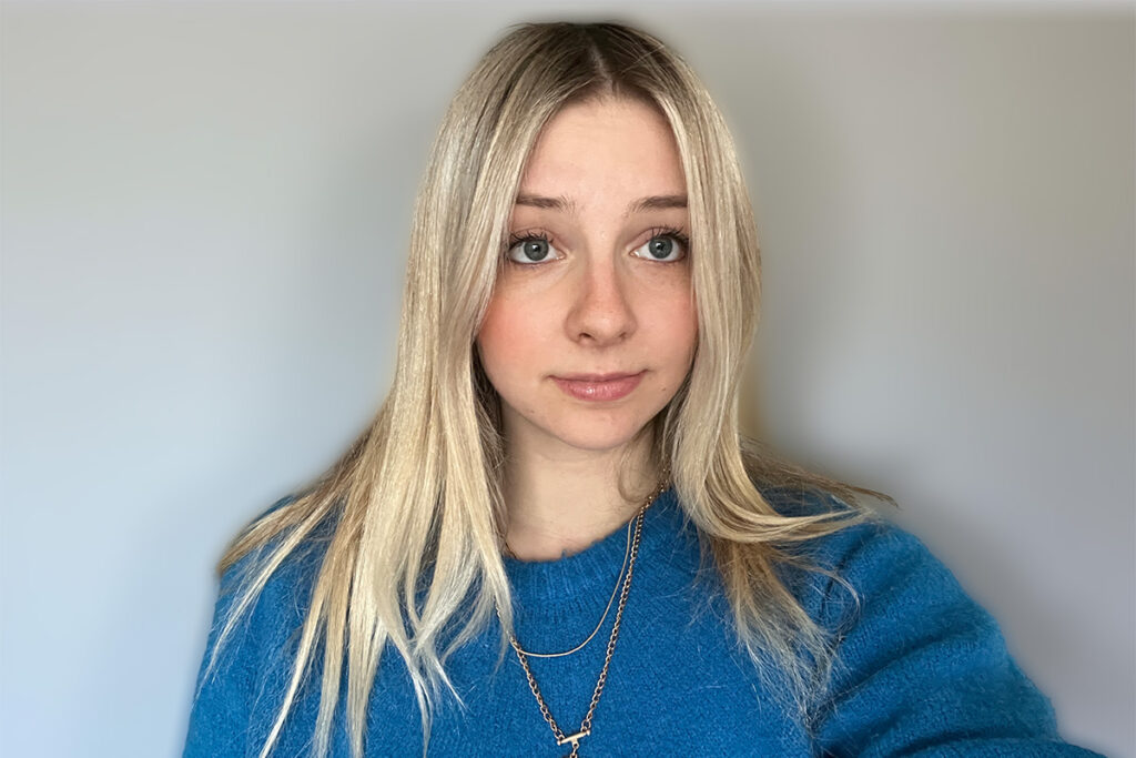 A woman with blonde hair, wearing a blue sweater, poses for a selfie.