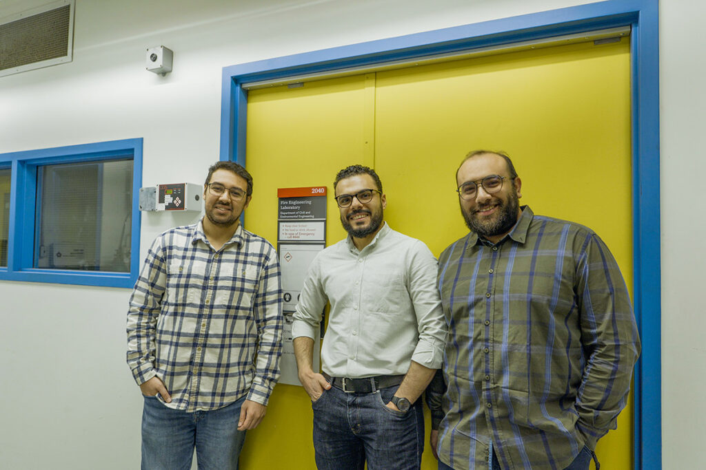 Three people pose for a group photo in front of a yellow door.