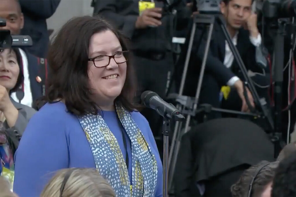 A woman wearing a blue shirt speaks into a microphone.