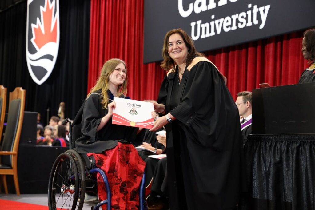 A graduating student, who uses a wheelchair, poses as she receives her degree