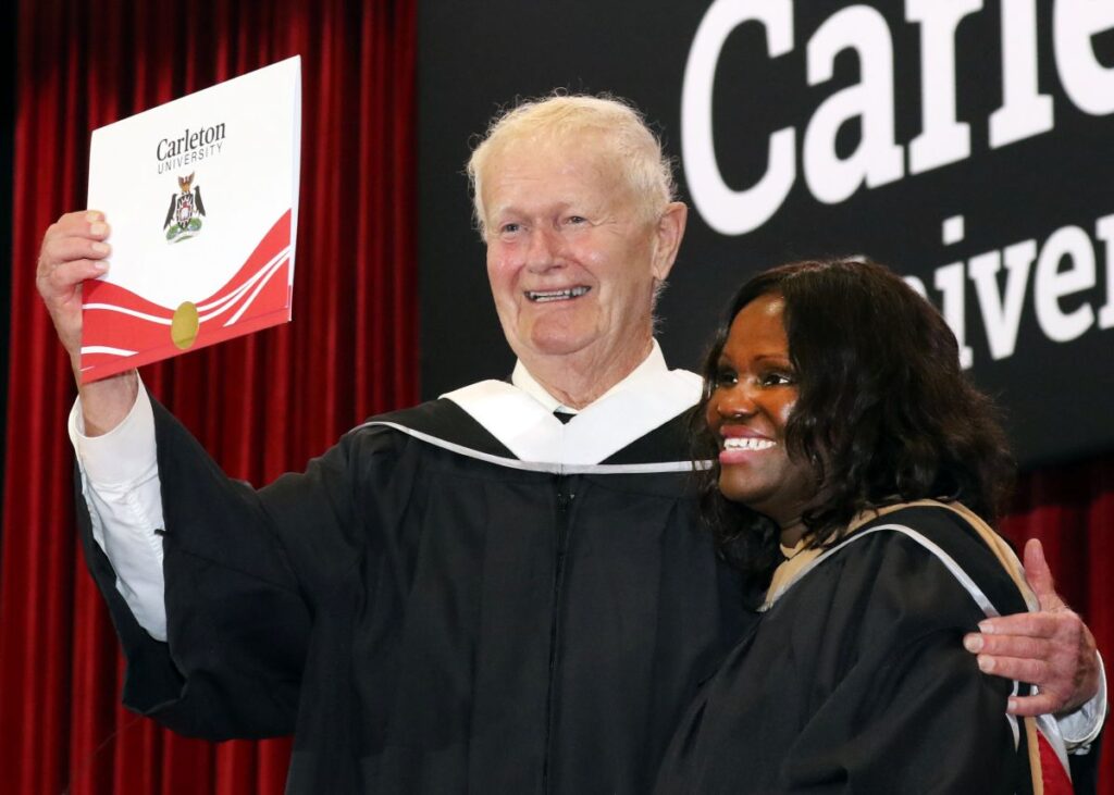 A graduating student raises his degree in celebration after crossing the stage
