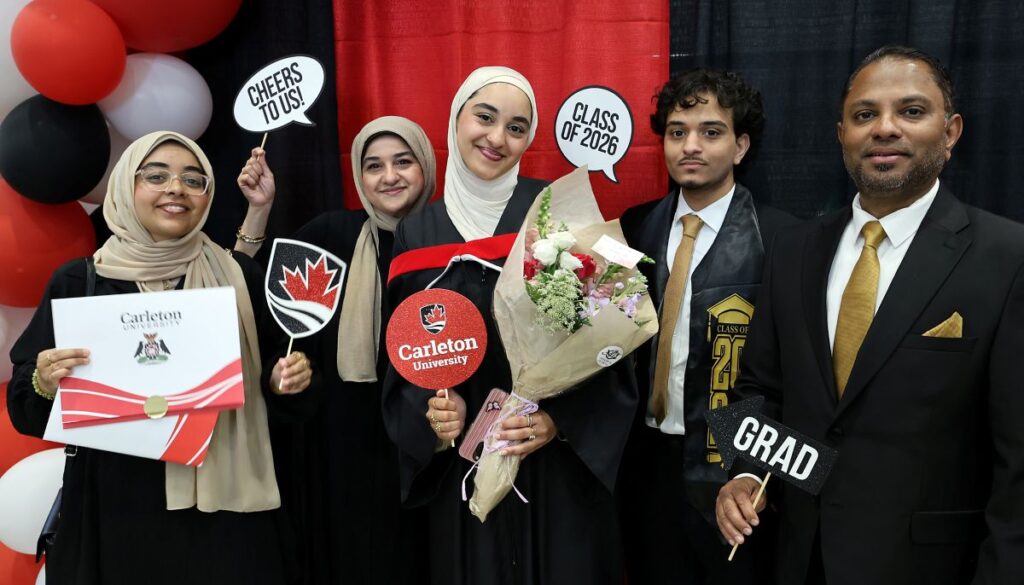 A graduating student and her four supporters pose with celebratory props and a bouquet of flowers