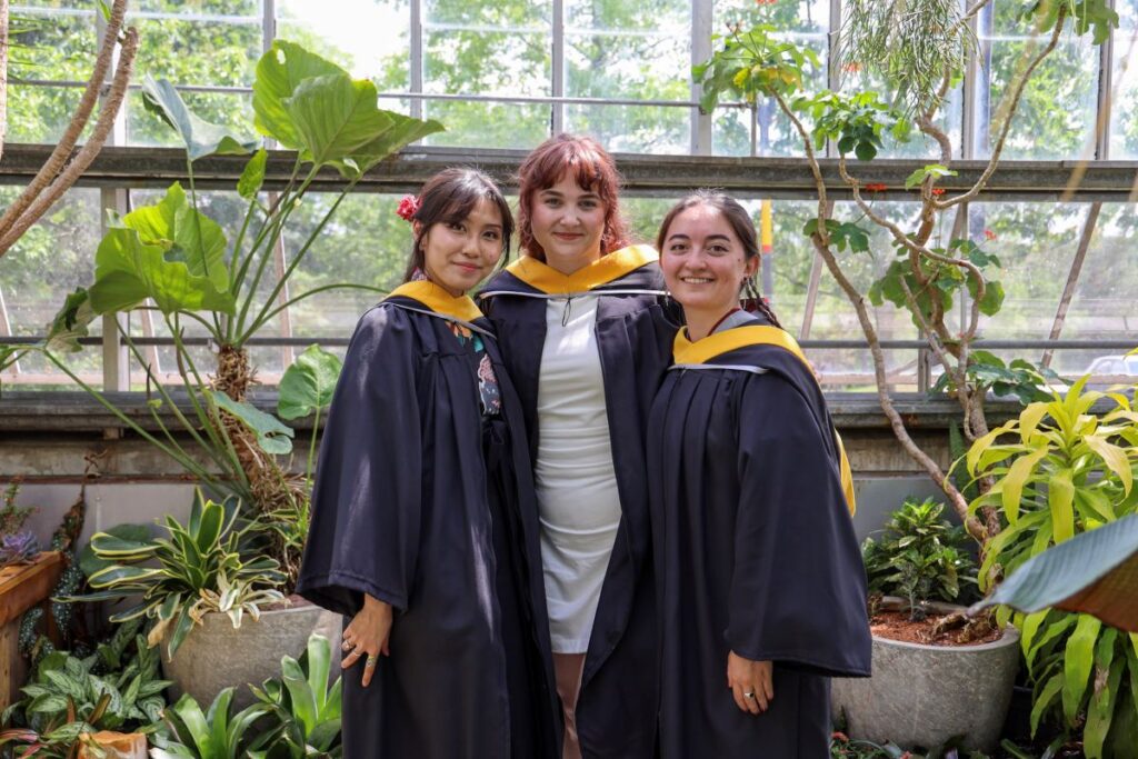 Three graduating students pose for a photo in the Nesbitt Greenhouse 