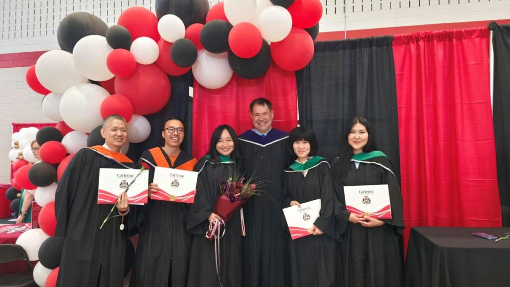 Five graduating students and a faculty member pose with their degrees.
