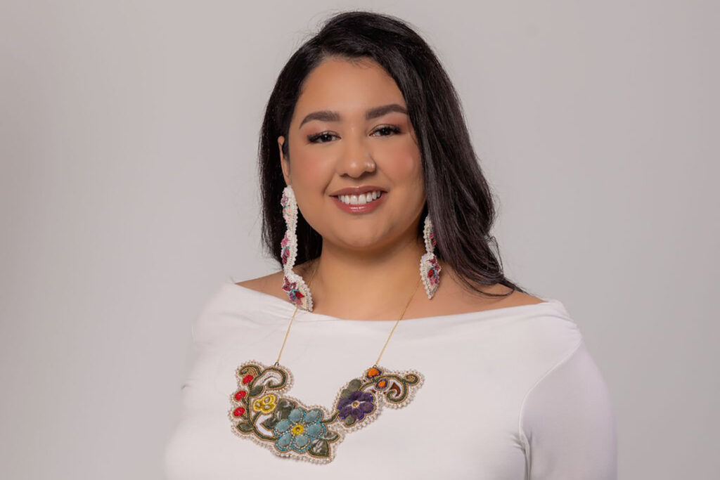 A professional headshot of a woman wearing a white shirt with a flowery design.