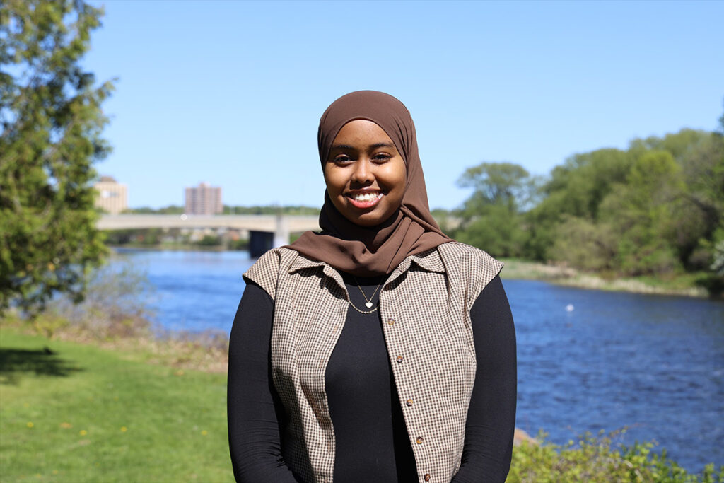 A woman poses for the camera while standing alongside a riverbank.