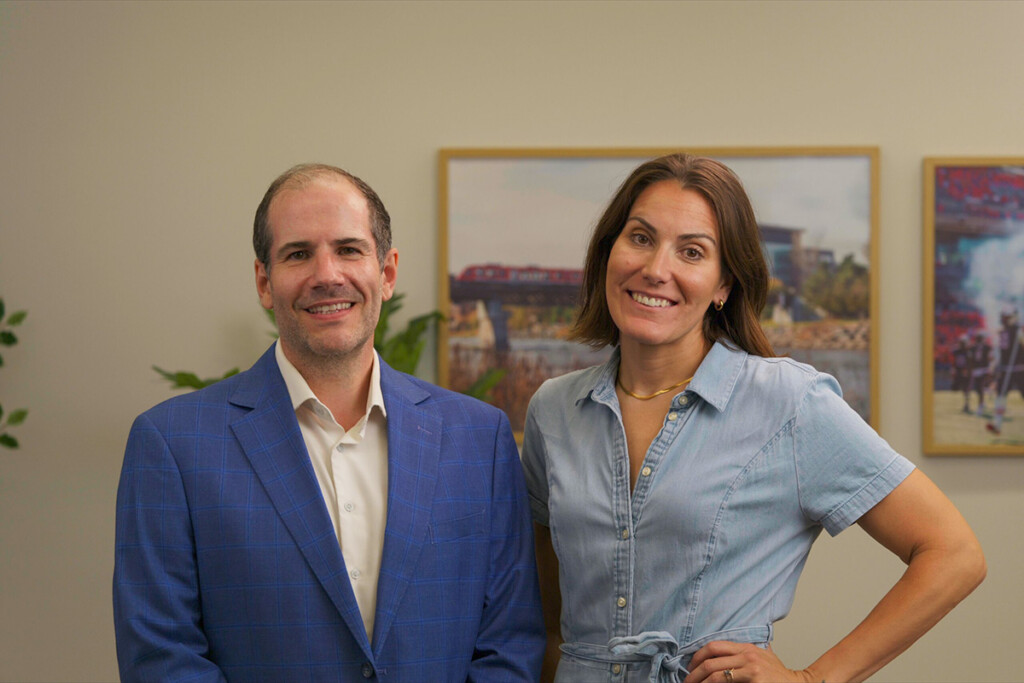 Alex Wilner and Leah West posing together for a photo in front of a large photo of the Carleton University campus.