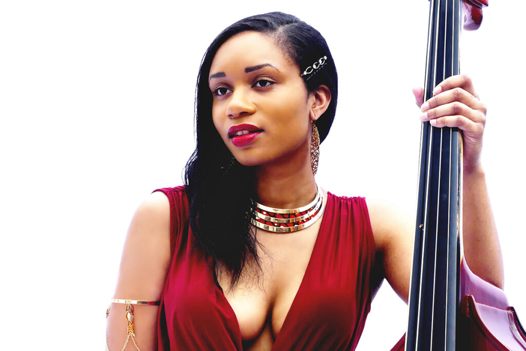 Singer Angelique Francis holds an instrument while wearing a red dress.