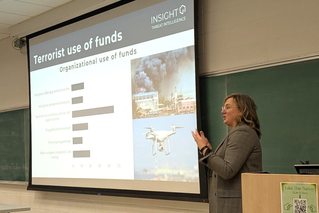 A woman stands at the front of a classroom while explaining data related to terrorists use of funds.